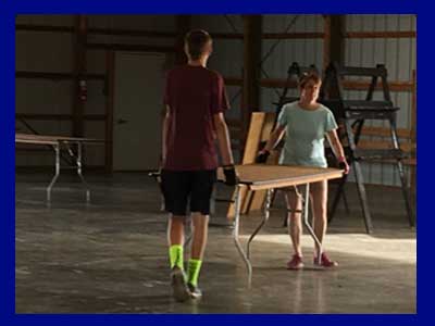 Two people carrying tables to setup for the fair